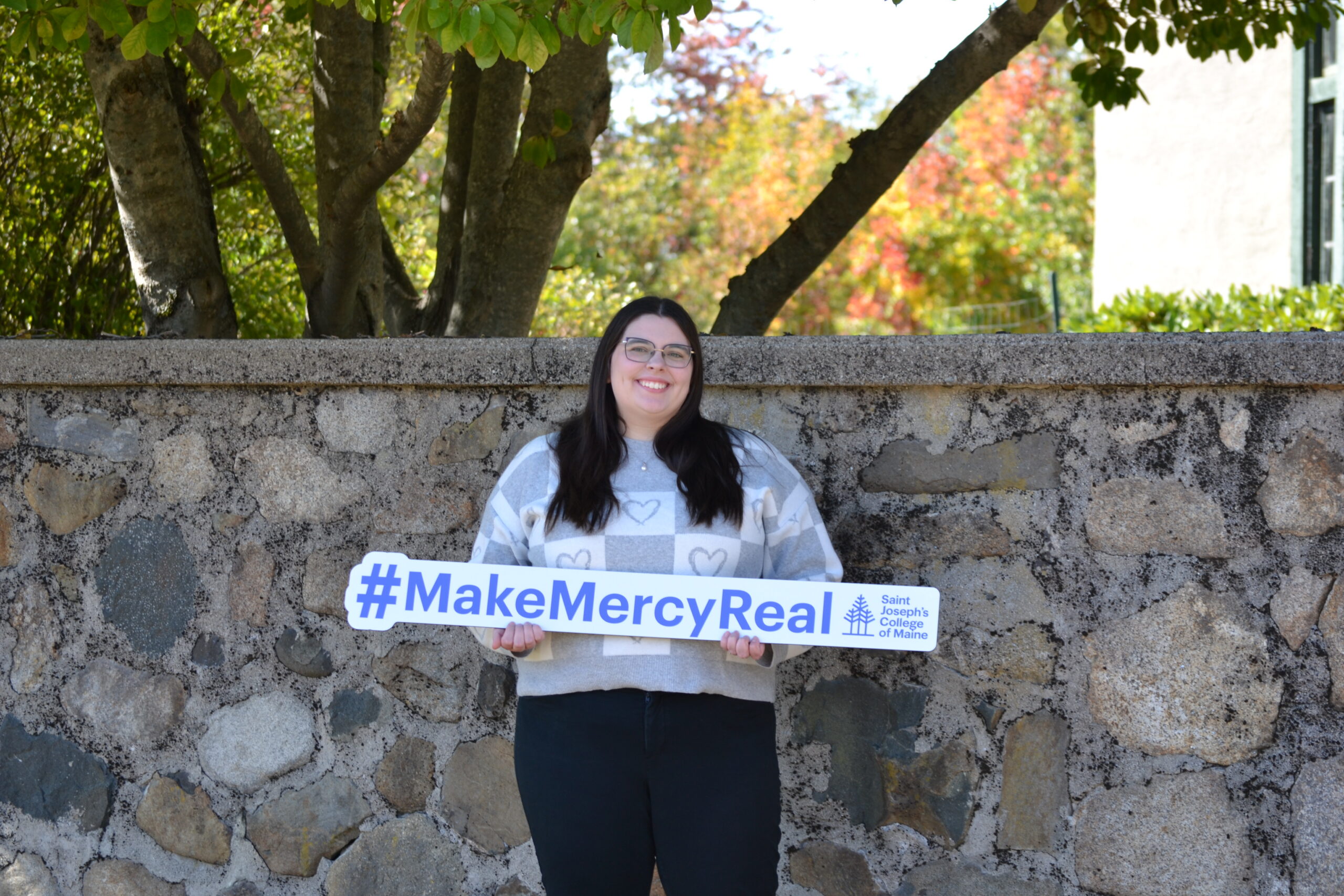 A person holds a sign that says #MakeMercyReal, highlighting the legacy of Saint Joseph’s College of Maine.
