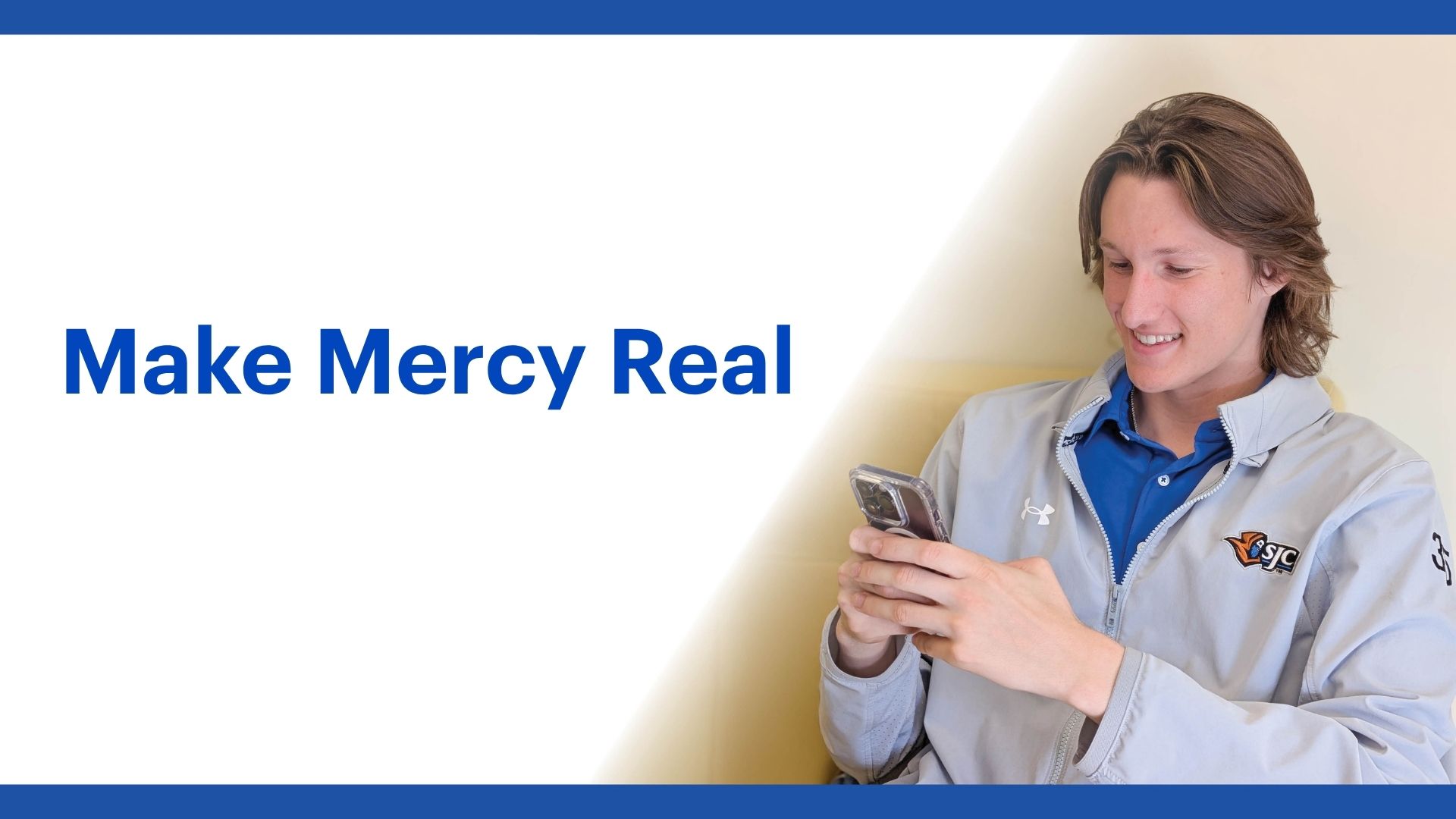A smiling person in a gray jacket looks at their phone. Beside them, bold blue text reads Make Mercy Real on a white background with blue borders, reflecting Saint Joseph’s College of Maine’s founding value of mercy.
